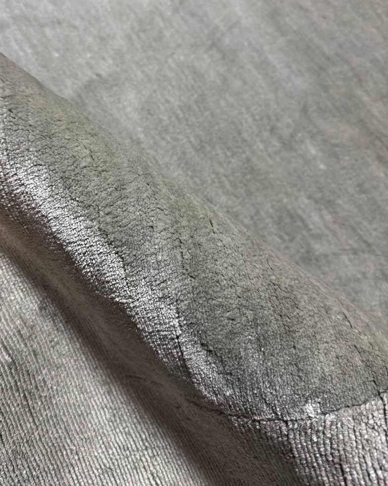 Close-up of a silver-grey rug with the edge folded back to show the dense, lustrous pile