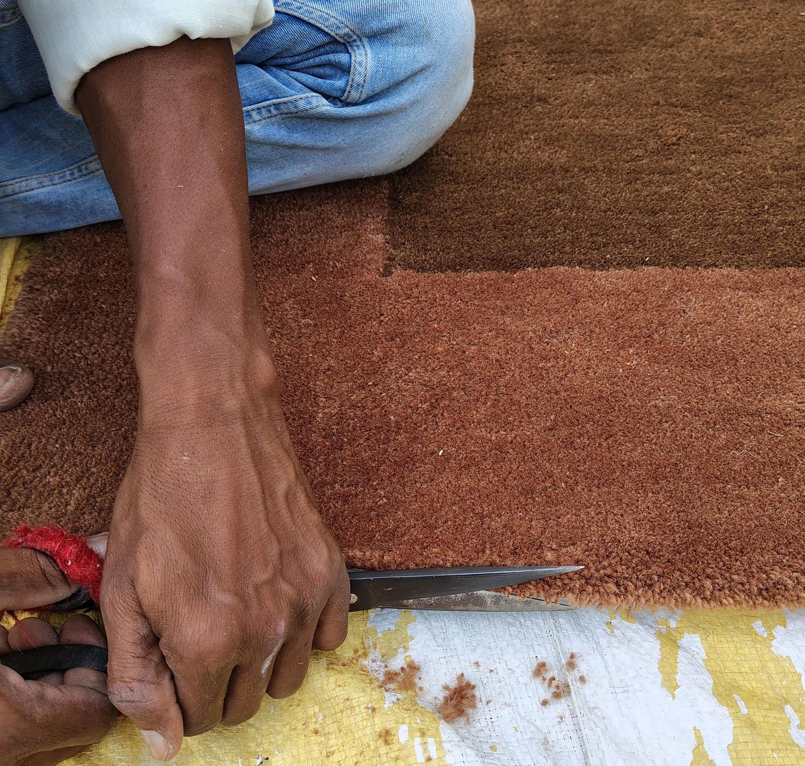 Hands carving the edge of a terracotta rug with shears