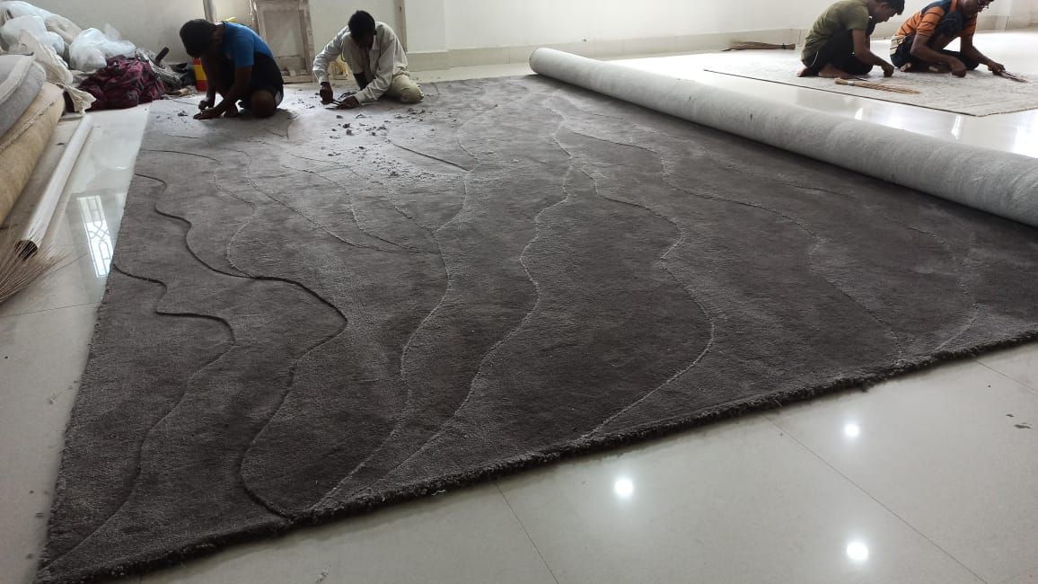 Four craftsmen finishing a large charcoal rug with a carved wave pattern