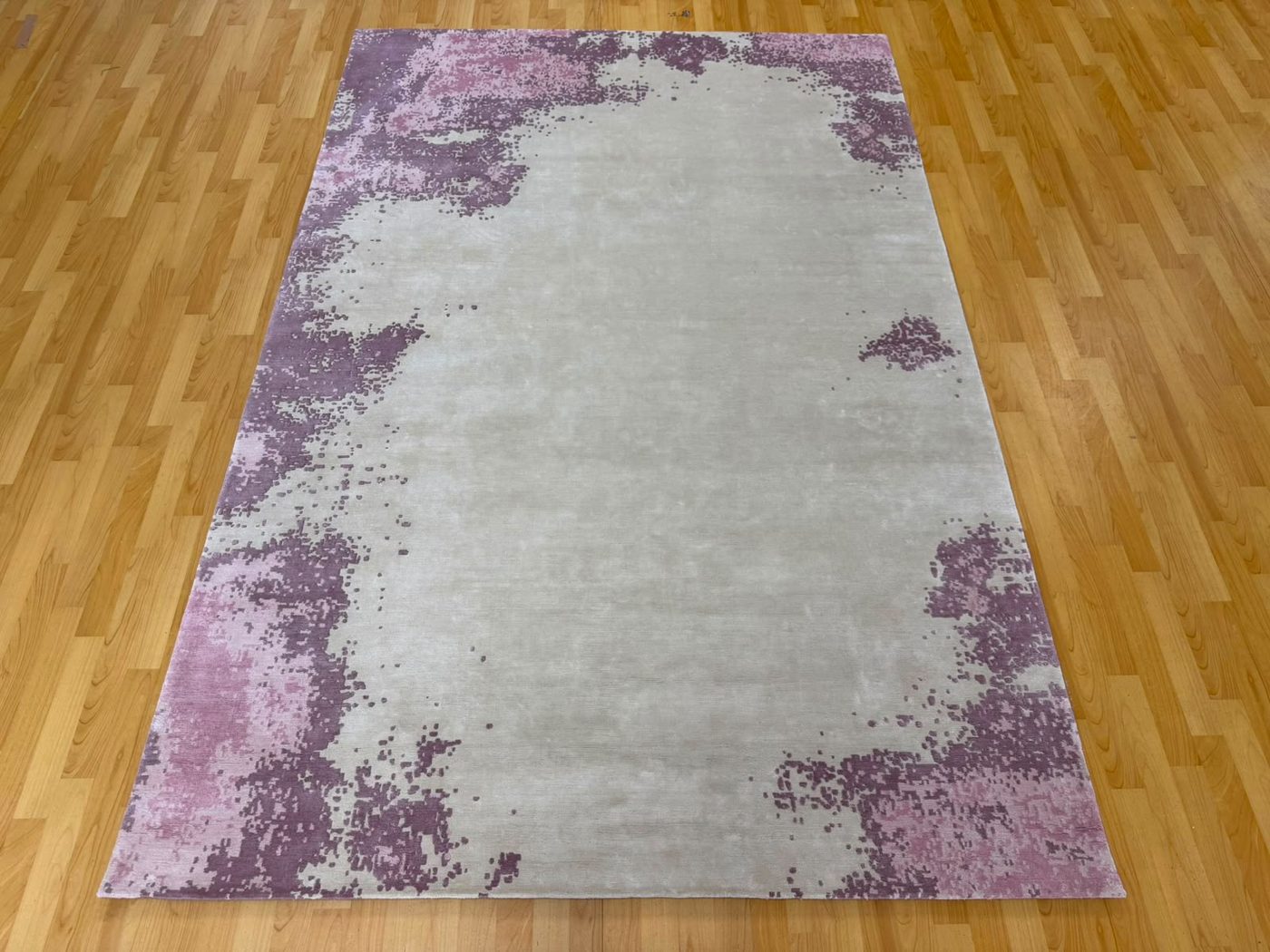 Finished ivory silk rug with violet and pink patterns along the edges