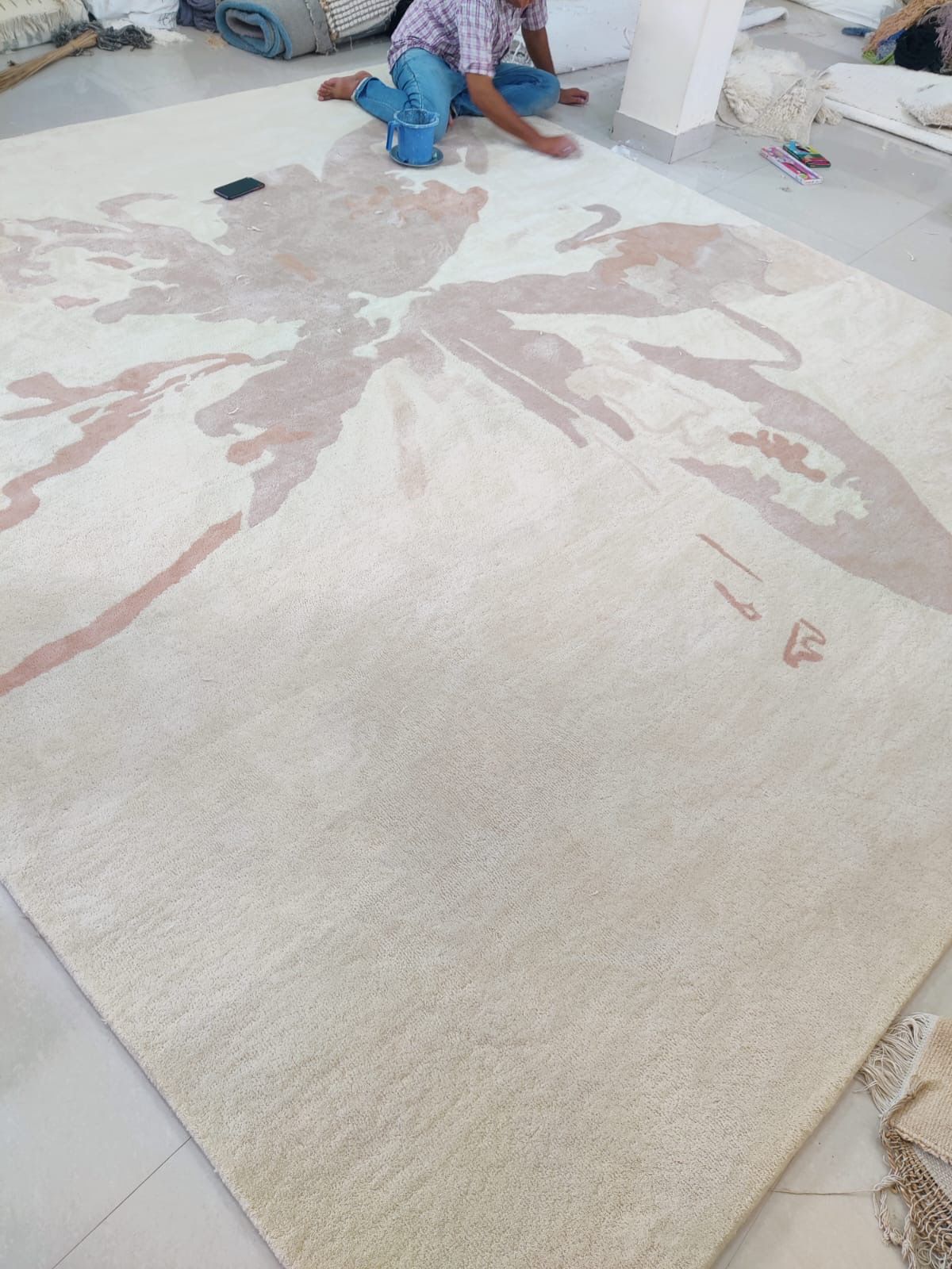 Large ivory rug with a blush butterfly motif, being finished by hand