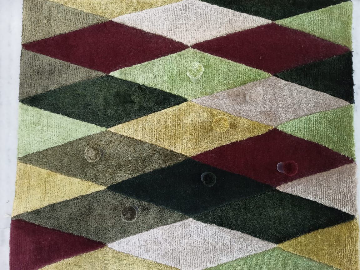Geometric rug of diamonds in green, burgundy, ochre and stone with colour poms on each shade